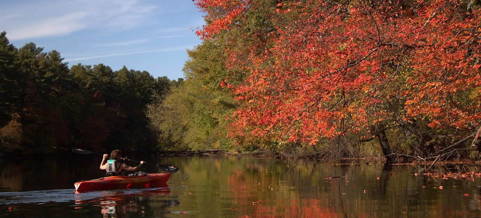 Kayak rouge sur une rivière calme bordée d'arbres aux feuilles d'automne